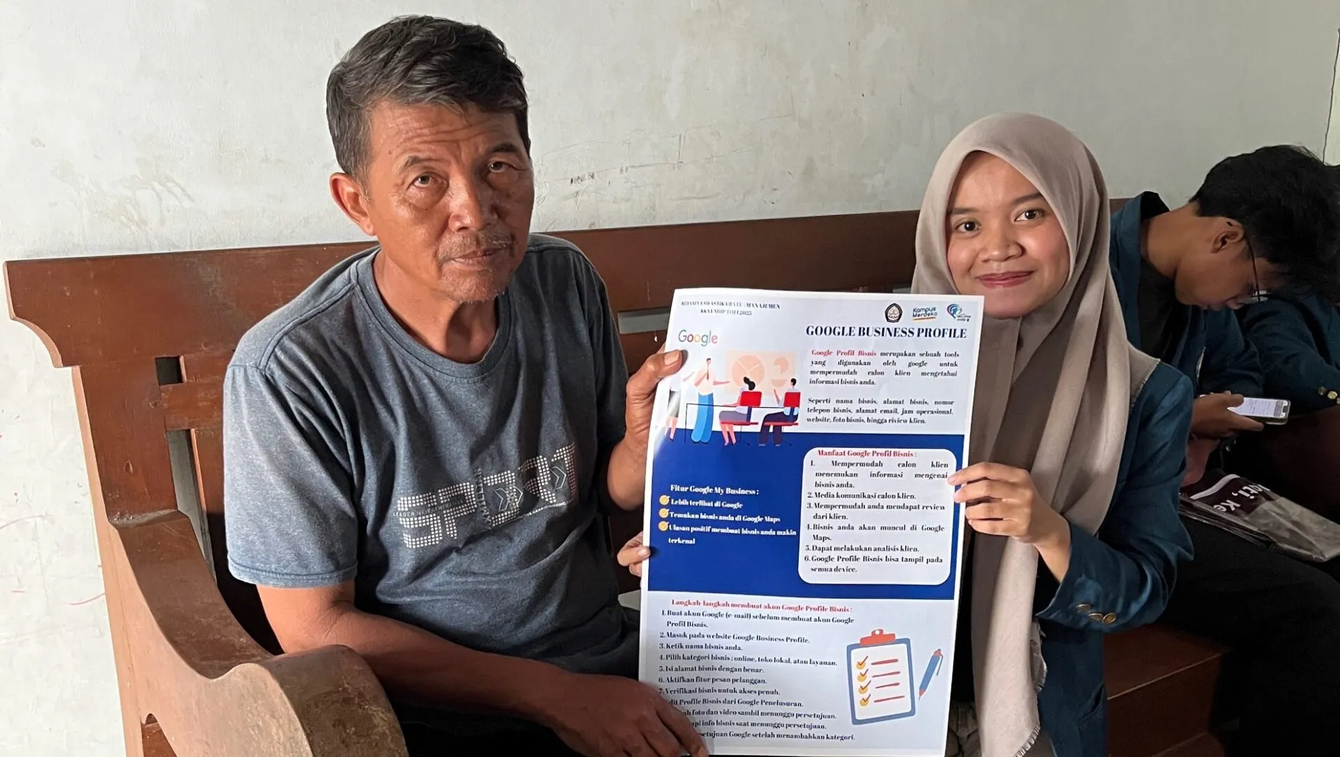 A person and person sitting at a table holding a blue bookDescription automatically generated